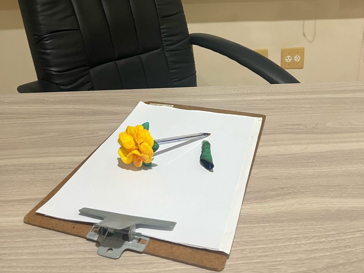 Prancheta com papel em branco e caneta sobre a mesa do consultório, diante da cadeira de atendimento