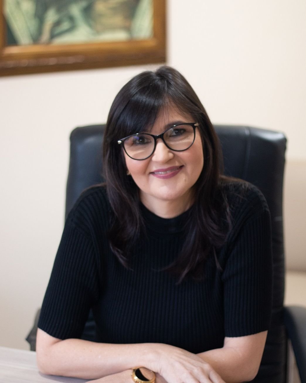 Maria Socorro de Menezes, psicóloga, sentada à mesa do consultório, de blusa preta
